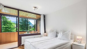 A bedroom with a large window, a bed, a bedside table with a lamp, and a view of greenery outside. - Riverview Apartment | Kitchen | Parking | Loggia (Bad Aussee)