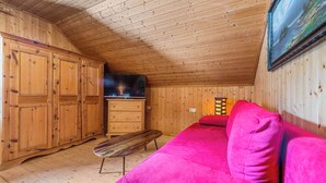 Ein Holzblockhaus im Inneren mit Holzbalkendecke, einem Fernseher, einem rosafarbenen Sofa und einer Holzbank.