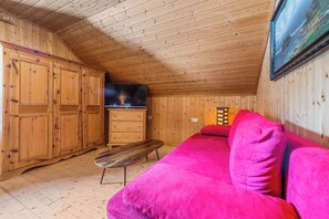 A wooden cabin interior with a wooden ceiling, a television, a pink sofa, and a wooden bench.