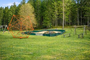 A geometric metal structure in a grassy field with trees in the background.
