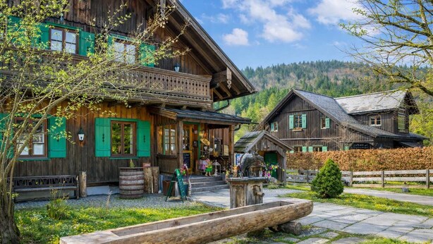 Ein traditionelles Holzhaus mit Balkon, einer hölzernen Bank und einem Steinweg.