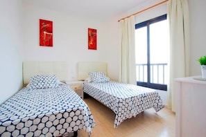 A hotel room with two beds, a nightstand, a window with curtains, and two wall art pieces. - Sara 4, Playa Blanca (Playa Blanca)