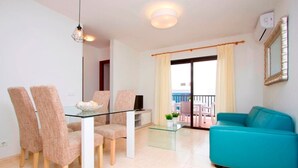 Ein modernes Wohnzimmer mit einem Glastisch, vier Stühlen, einem türkisfarbenen Sofa und einem Balkon mit Blick.