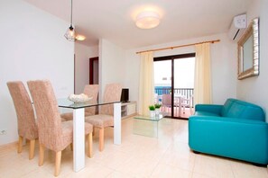 Una sala moderna con una mesa de comedor de cristal, cuatro sillas, un sofá color turquesa y un balcón con vistas.