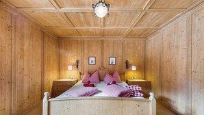 A wooden-paneled room with a bed, two bedside tables, and a hanging light fixture.