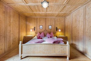 A wooden-paneled room with a bed, two bedside tables, and a hanging light fixture.