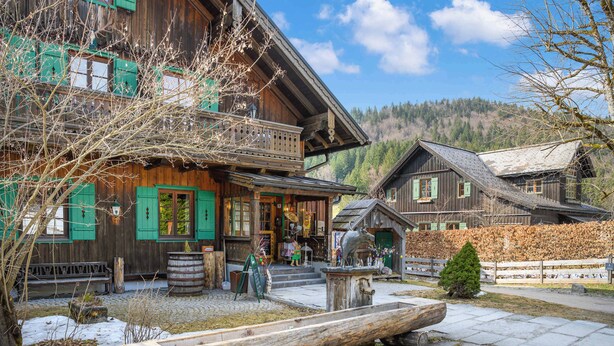 A wooden building with a balcony, a wooden bench, and a small tree in front.