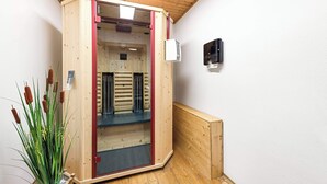 A sauna with a wooden interior, a glass door, and a small plant beside it.