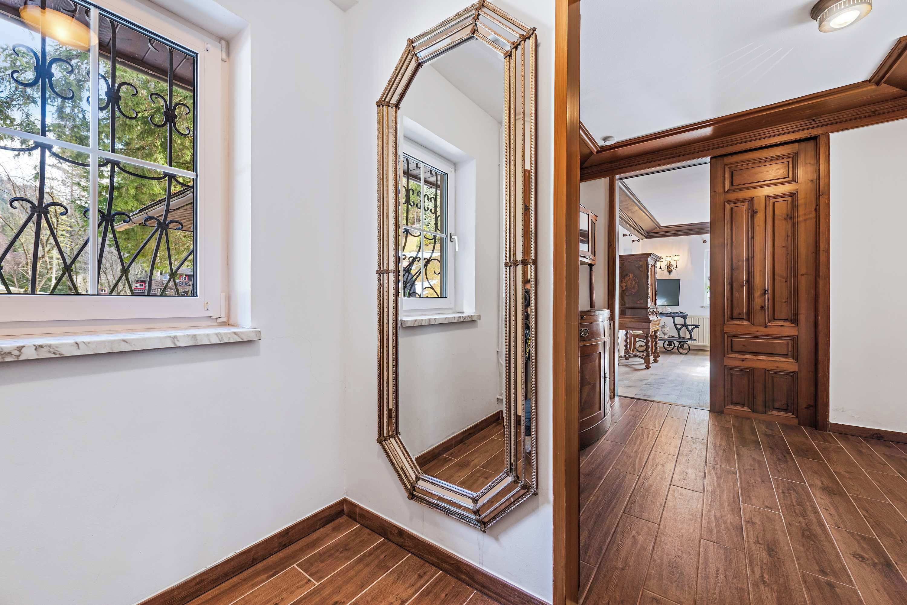 A hallway with a large mirror, wooden flooring, and a view into a dining area.