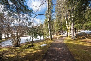 Un sentier pavé dans un parc, avec des arbres et une étendue d’eau en arrière-plan.
