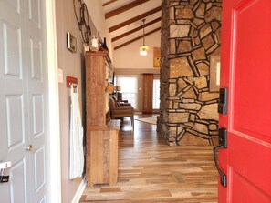 A hallway with a stone wall, wooden flooring, and a red door.