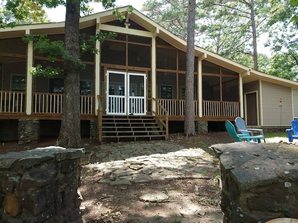A cabin with a wooden deck, stone pathway, and a porch with chairs.