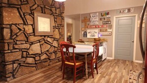 Ein Essbereich mit Steinwand, Holzsesseln, einem Tisch und einer Küche im Hintergrund.