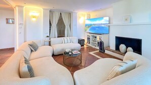 Un salon moderne avec un canapé d’angle, un téléviseur à écran plat, une cheminée et une vue sur la mer.