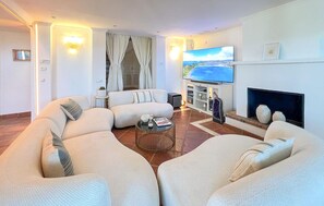 A modern living room with a sectional sofa, a flat-screen TV, a fireplace, and a view of the sea. - Amazing home in Benahavis with private swimming pool, can be inside or outside (Benahavis)