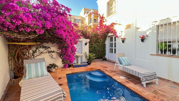 Un espace piscine comprenant une petite piscine, deux chaises longues et une pergola ornée de fleurs roses.