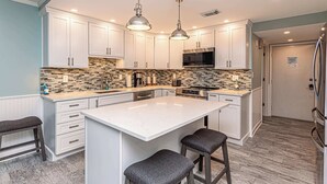 Una cocina moderna con armarios blancos, una isla grande, iluminación colgante y un microondas.