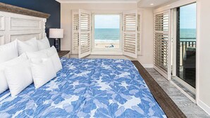 Un dormitorio con una cama grande, un ventilador de techo, vista a la playa y un balcón con barandilla.