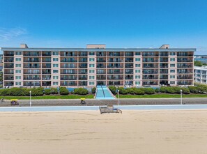 Ein mehrstöckiges Hotel mit einer zentralen Treppe, Balkonen und Blick auf den Strand.