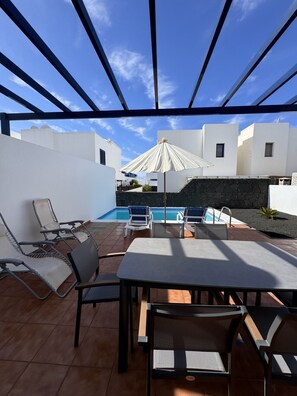 A poolside area with a pergola, lounge chairs, a table, and a pool. - Papagayo House, Playa Blanca (Playa Blanca)