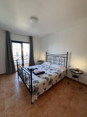 Ein Schlafzimmer mit einem Bett, zwei Nachttischen, einem Fenster mit Vorhängen und Blick ins Freie.