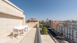A balcony with a table and chairs, overlooking a cityscape with buildings and a clear sky. - Guestready - Republic Apartments (Lisbon)