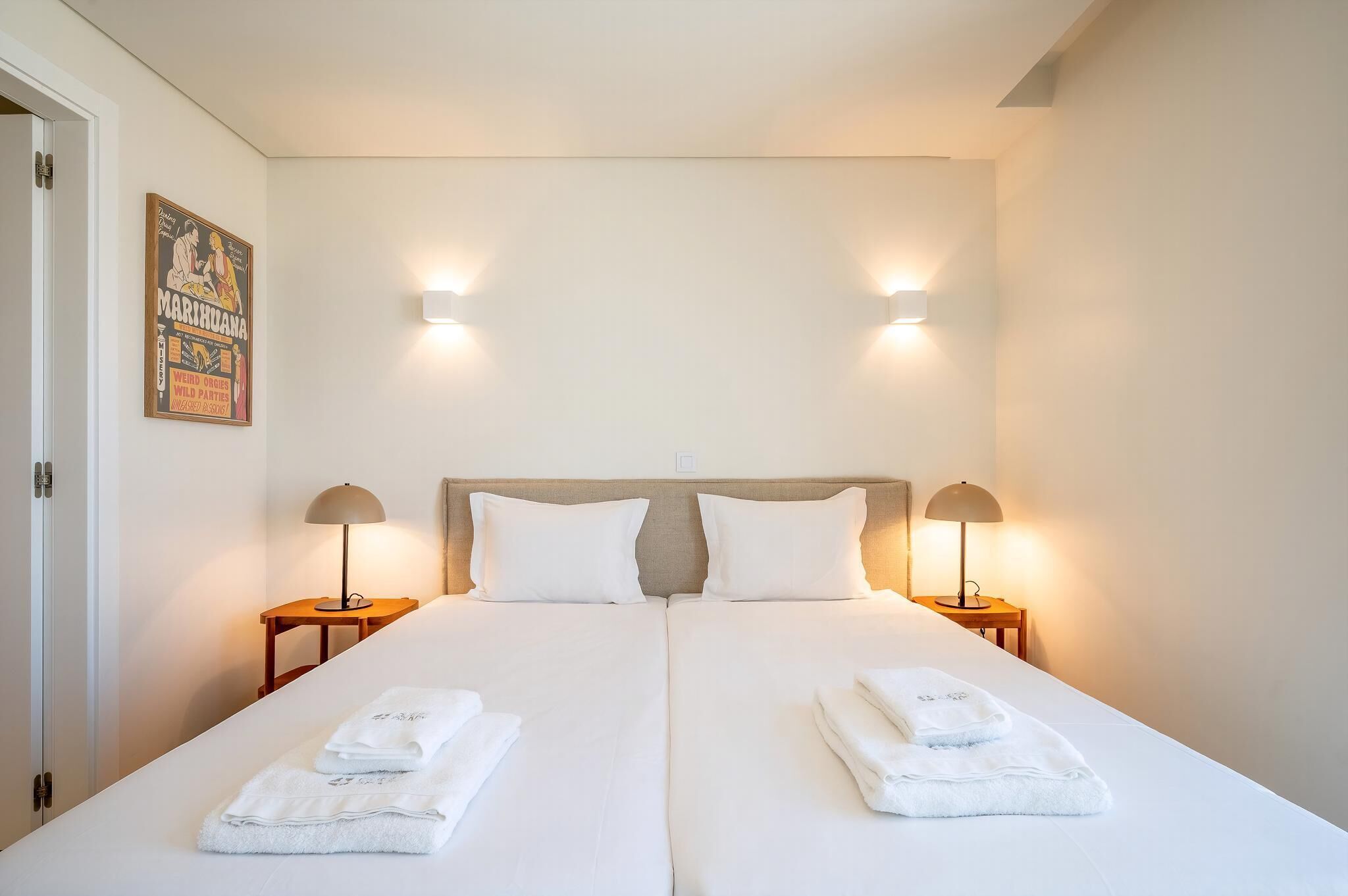 Un lit double avec du linge de lit blanc, deux lampes de chevet et une affiche accrochée au mur.