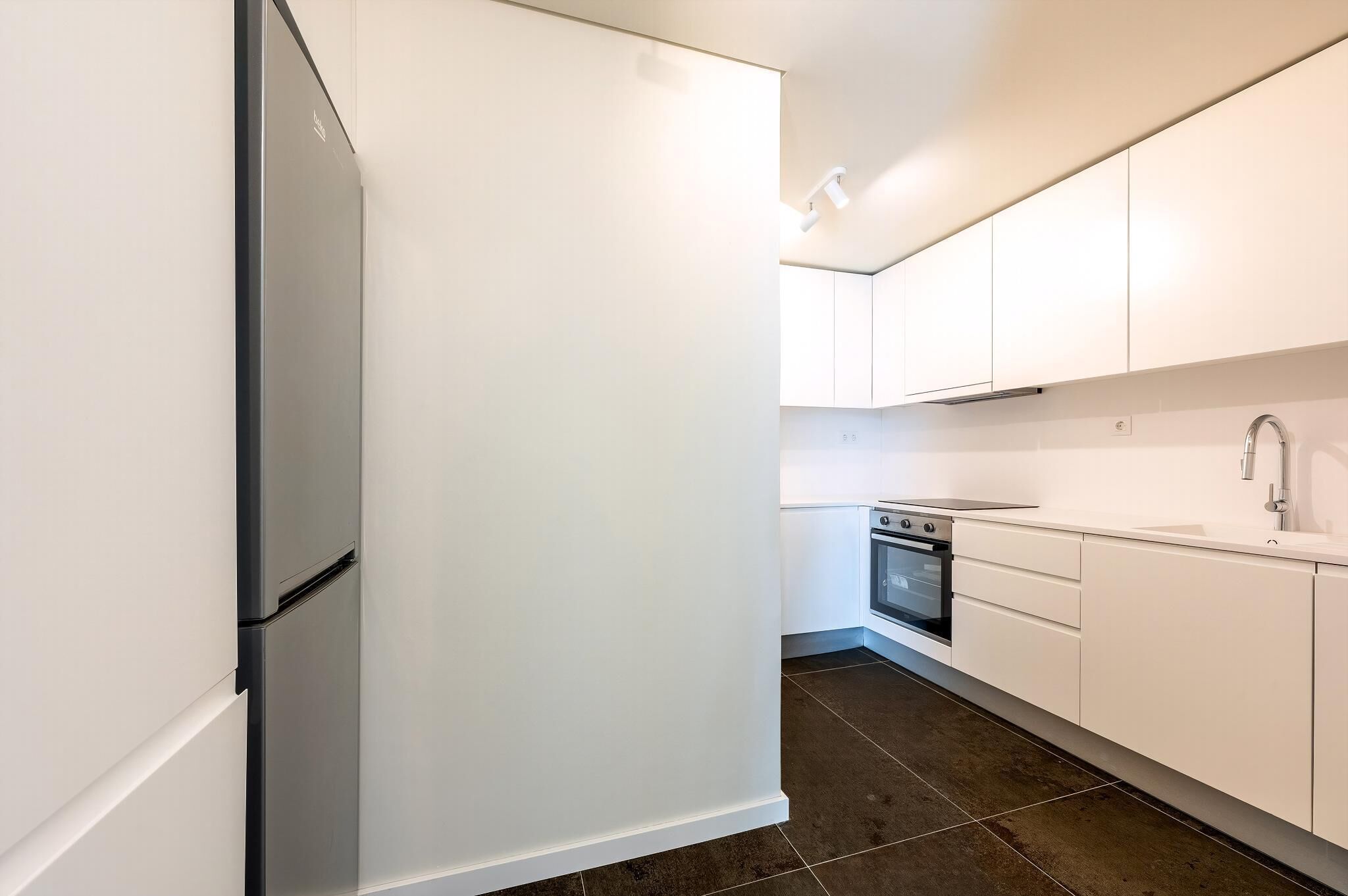 A modern kitchen with white cabinetry, a stainless steel refrigerator, a built-in oven, and a sink.