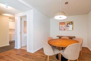 Un comedor con una mesa redonda de madera, seis sillas tapizadas, una lámpara colgante y dos carteles en la pared.