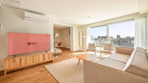 A modern living room with a large TV, a sofa, a coffee table, and a view of the city through large windows. - Guestready - Republic Apartments (Lisbon)