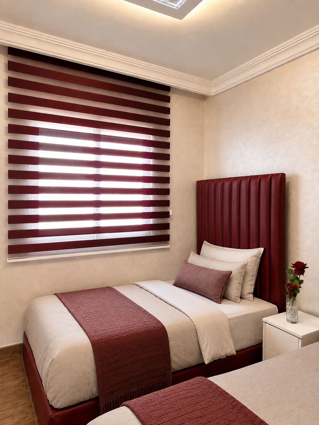 A bedroom with a bed, a nightstand, a vase with flowers, and a window with blinds.