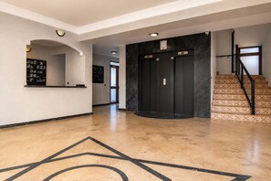 Eine Lobby mit einer Rezeption, einem schwarzen Aufzug und einer Treppe.