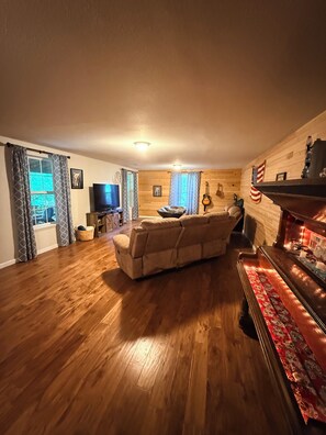 A living room with a sofa, a television, a fireplace, and a wooden floor.