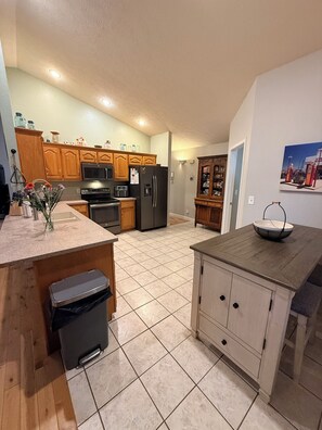 A kitchen with wooden cabinets, a refrigerator, an oven, and a trash bin.
