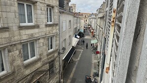 Une rue étroite bordée d’immeubles anciens en pierre, dont les fenêtres et les portes sont bien visibles, avec quelques piétons et des vélos garés.