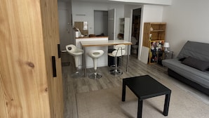 Un espace de vie moderne comprenant un coin cuisine, une table à manger avec quatre chaises, un canapé et une armoire en bois.