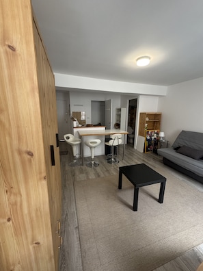 Ein moderner Wohnbereich mit Küchenzeile, einem Esstisch mit vier Stühlen, einer Couch und einem Holzschrank.