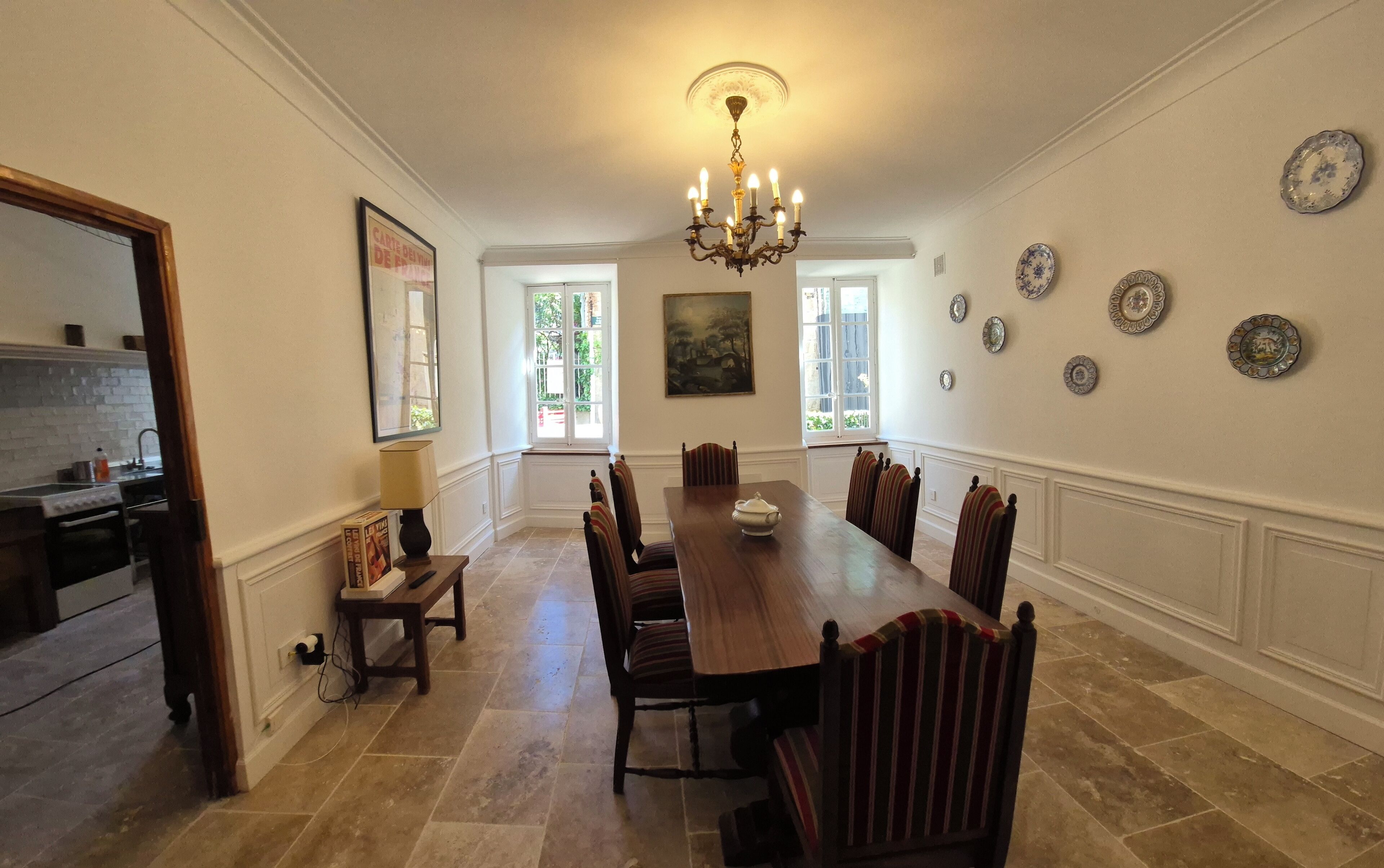 Ein Esszimmer mit einem langen Holztisch, sechs Stühlen, einer Chandelier und einem Gemälde an der Wand.