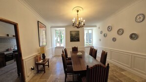 A dining room with a long wooden table, six chairs, a chandelier, and a painting on the wall.
