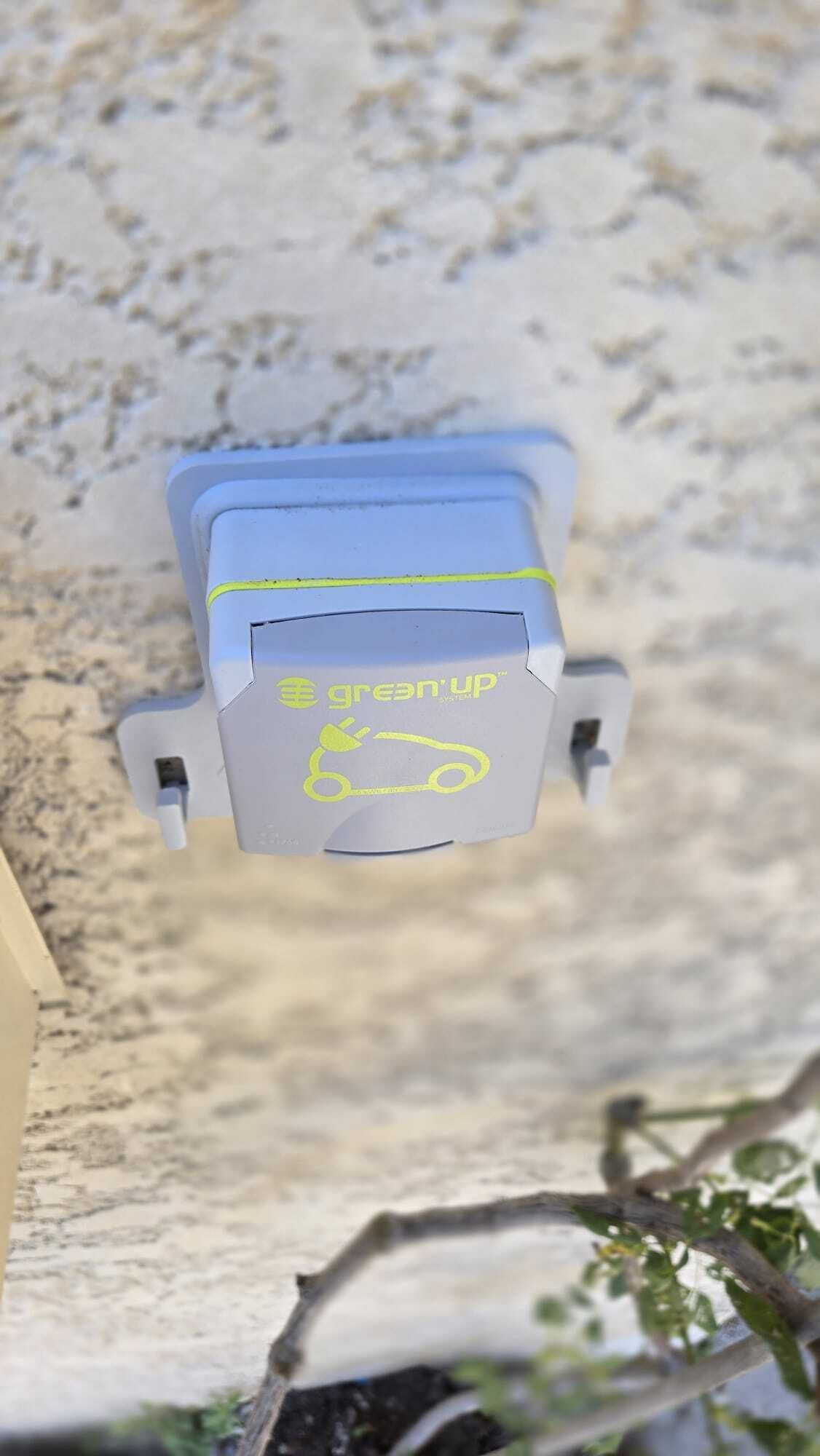 A gray electrical box with a green stripe and a logo that reads 'greenup' on a textured wall.