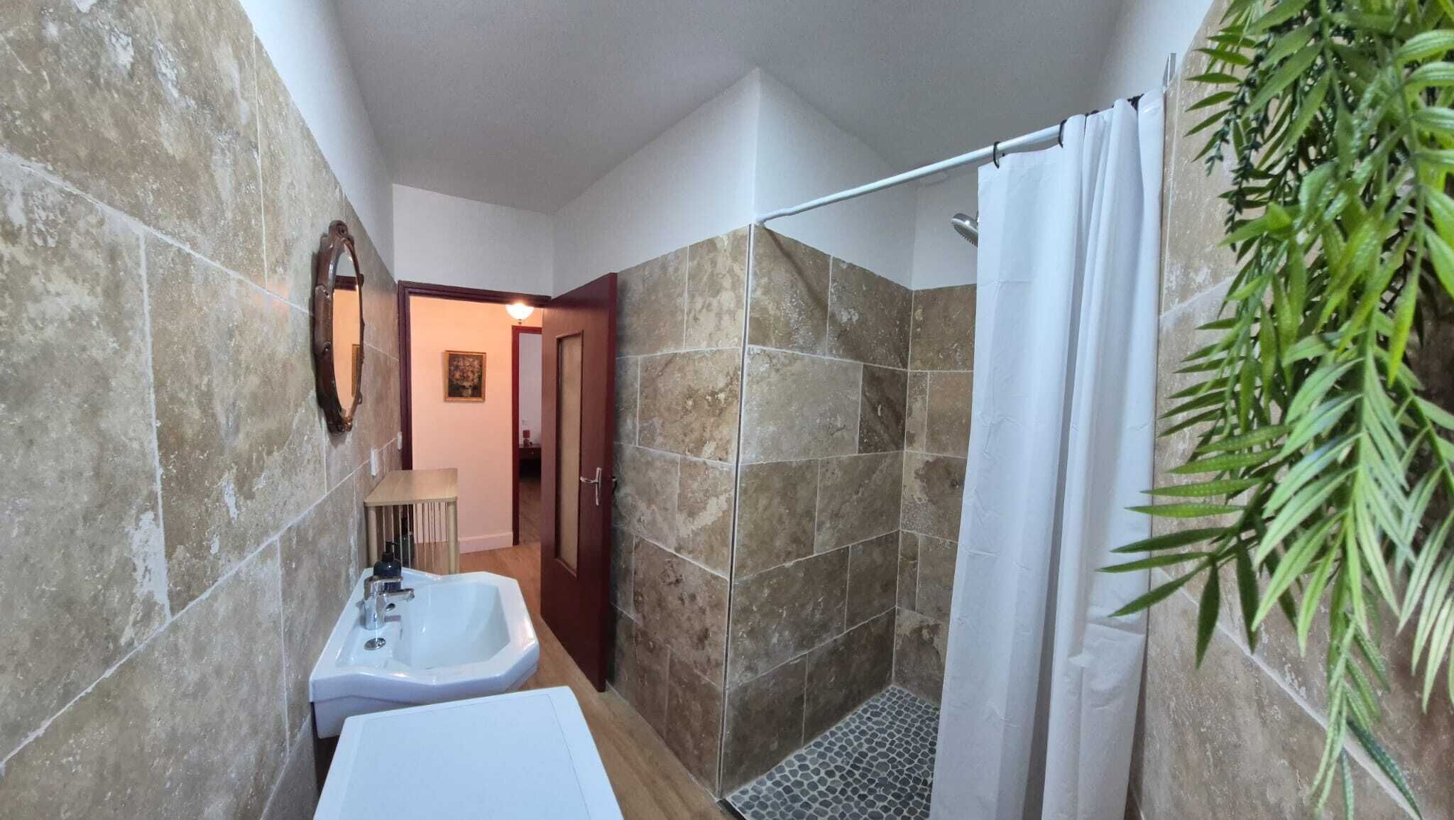A bathroom with a shower, a sink, a mirror, and a door leading to another room.