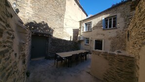 A narrow courtyard with stone walls, a table with chairs, and a door.