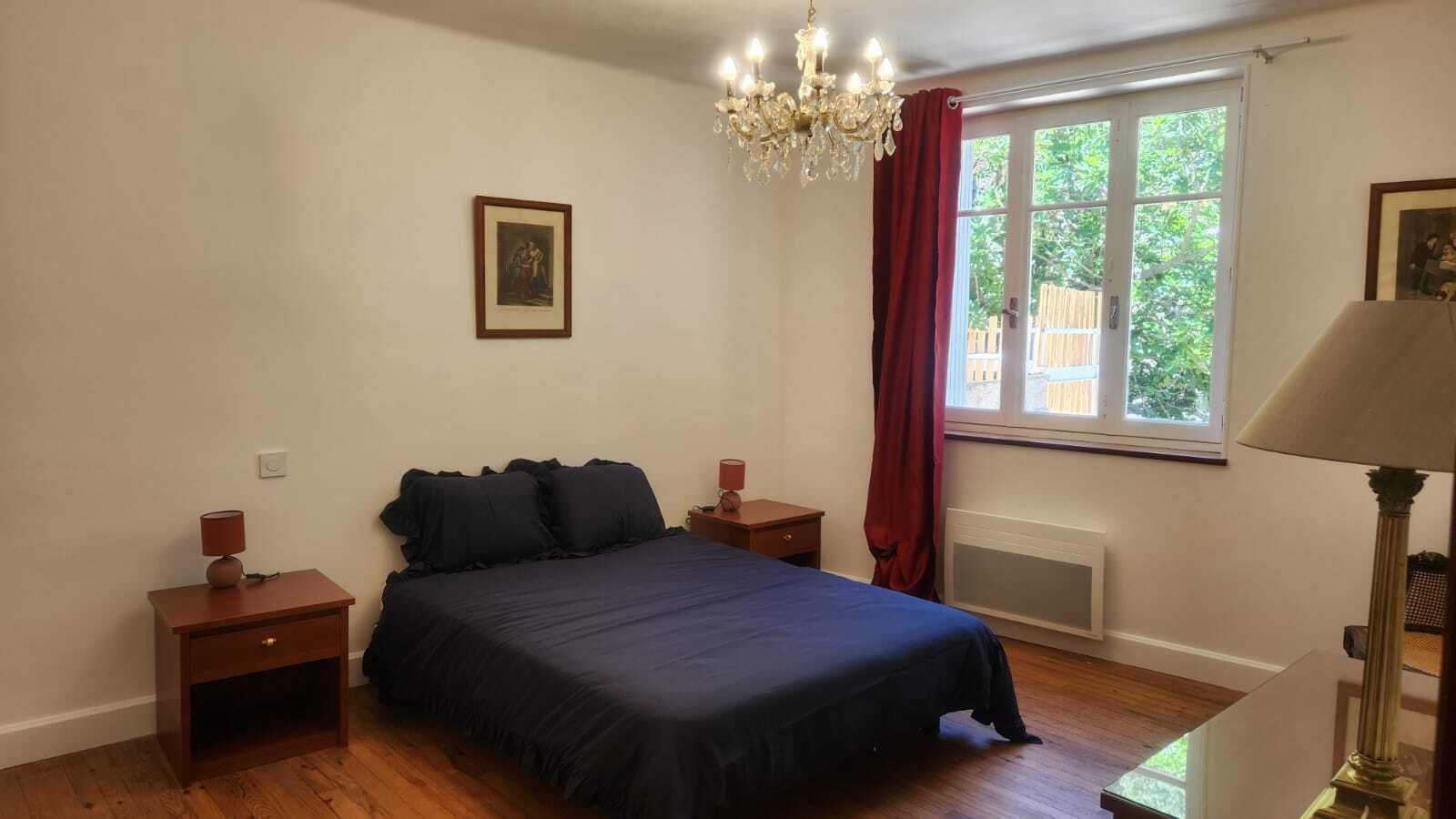 Een slaapkamer met een bed, nachtkastjes, een kroonluchter, een raam met gordijnen en een radiator.