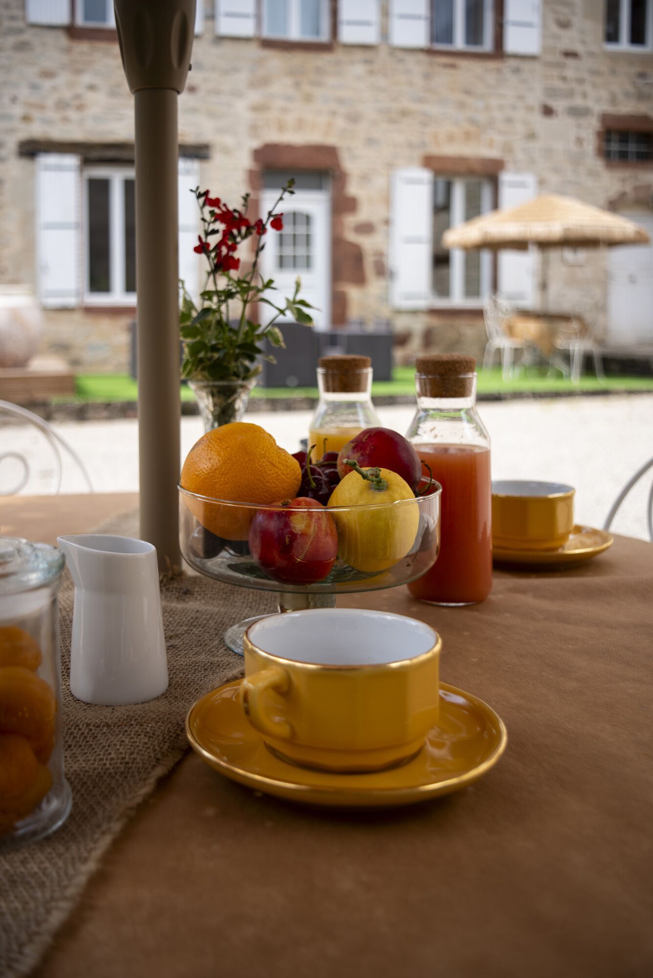 A breakfast table with a fruit bowl, a yellow cup, a glass pitcher, and a bottle of juice.