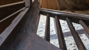Puinen, spiraalimainen portaikko, jossa on metallinen kaide ja pieni ikkuna yläosassa.