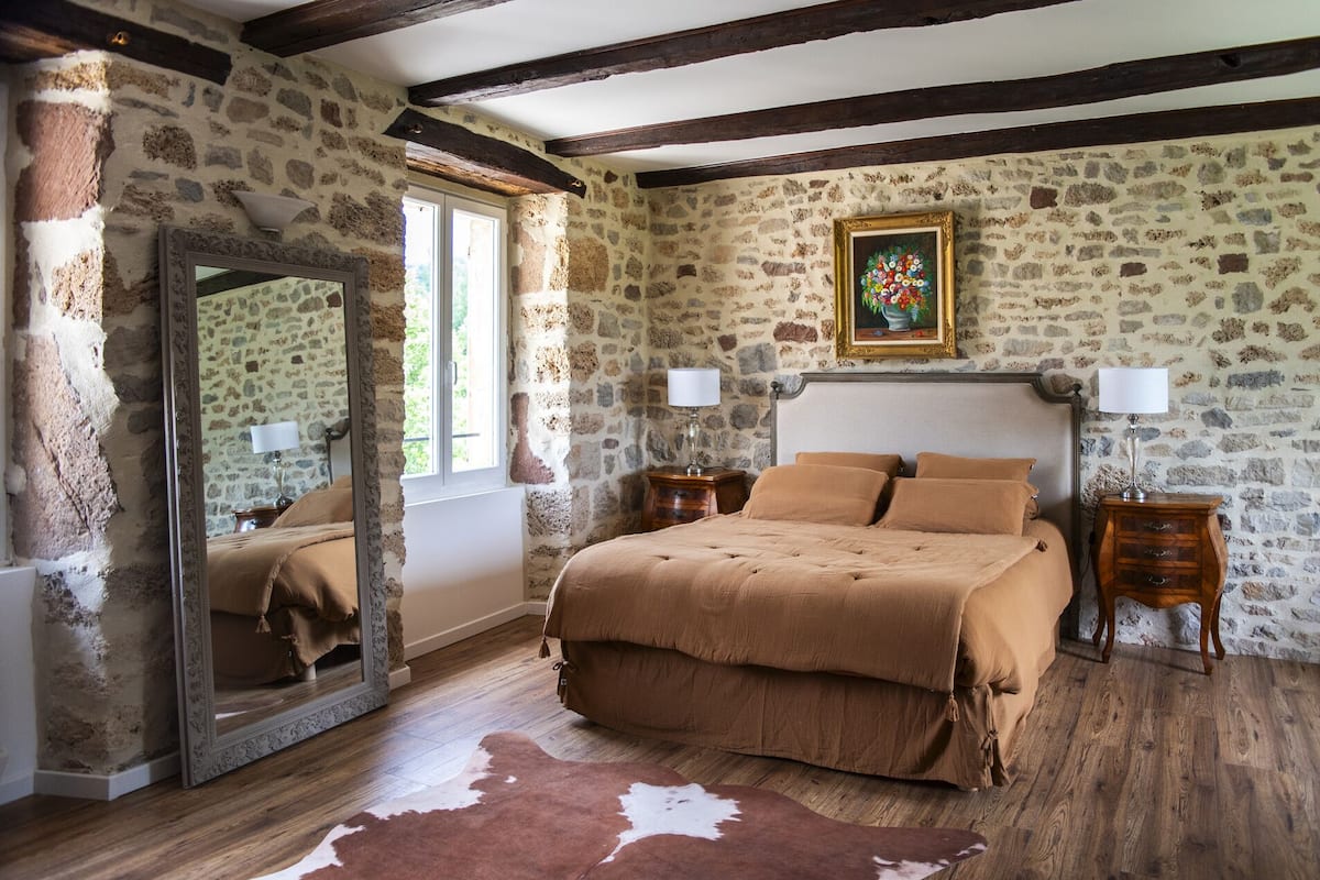 Un dormitorio con paredes de piedra, una cama de madera, un espejo y un cuadro.