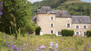 A stone building with multiple windows and a garden with purple flowers.