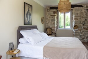 Un dormitorio con cama, ventana con vistas, pared de piedra y un cuadro en la pared.