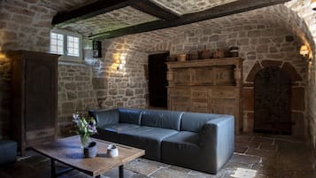A stone-walled room with a leather sofa, a wooden table with a vase, and a cabinet with baskets.