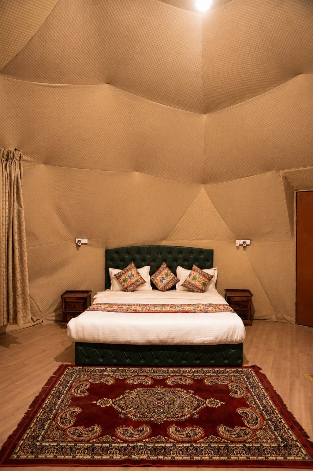 A bedroom with a bed, pillows, a nightstand, a wall-mounted lamp, and a patterned rug.